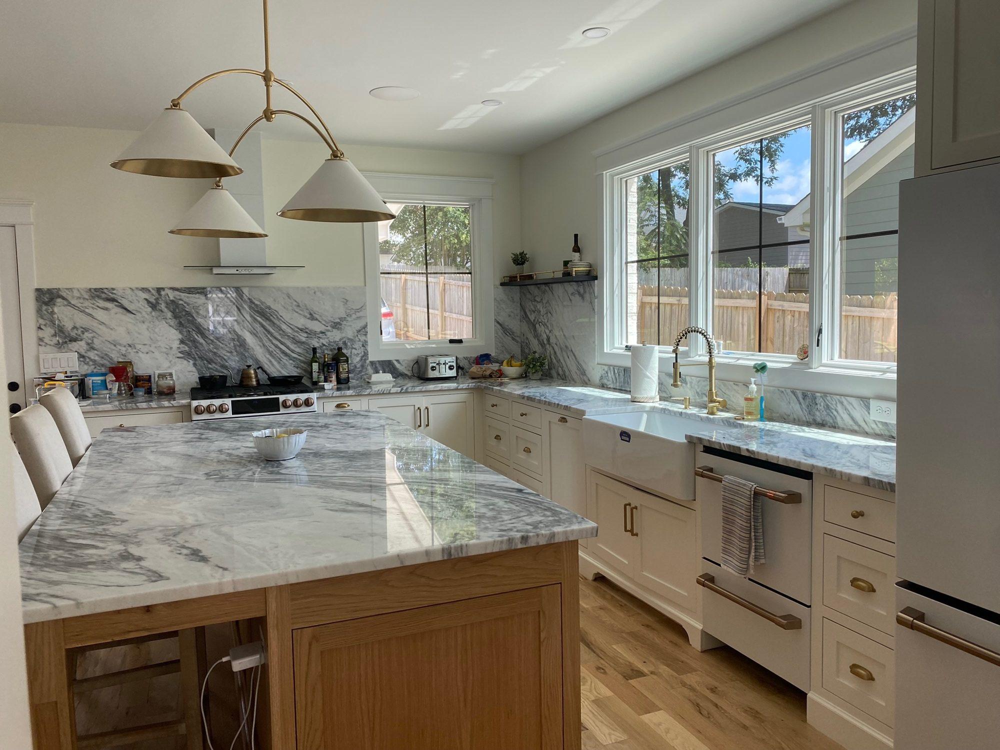 Kitchen with full-height marble backsplash and countertops, white inset cabinetry, brass hardware, and a white oak island.